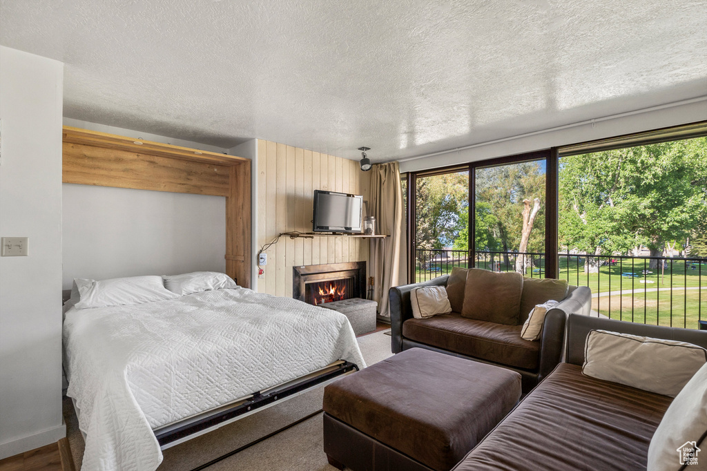 Bedroom with multiple windows, a lit fireplace, a textured ceiling, and access to exterior