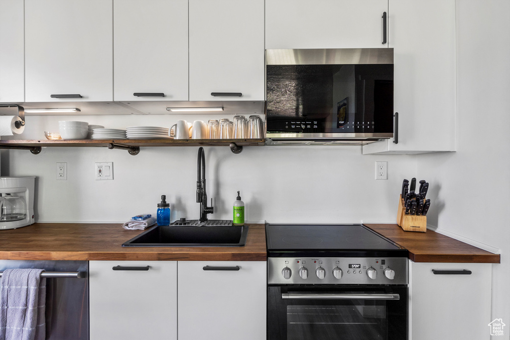 Kitchen with butcher block counters, stainless steel appliances, open shelves, and white cabinetry