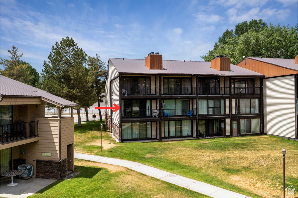 Back of house with a chimney, a balcony, a lawn, and stone siding
