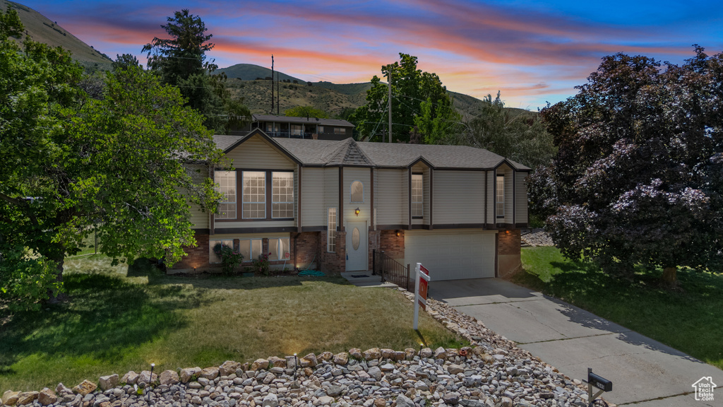 Bi-level home with brick siding, concrete driveway, a garage, and a yard