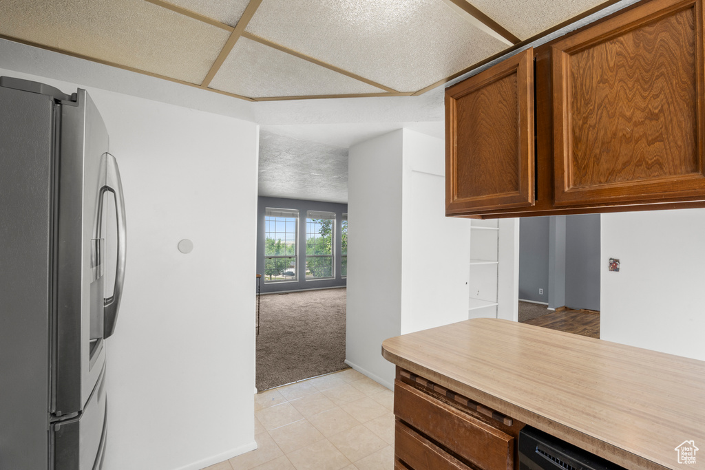 Kitchen featuring freestanding refrigerator, light countertops, light colored carpet, brown cabinets, and light tile patterned flooring