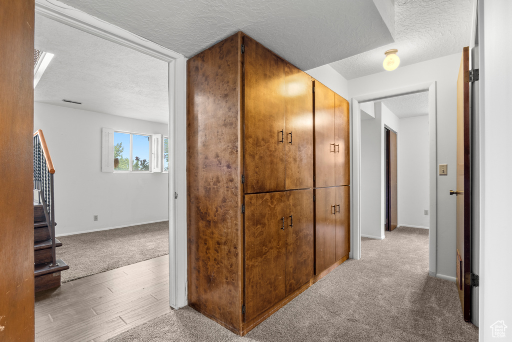 Hall featuring a textured ceiling, carpet floors, stairs, and wood finished floors