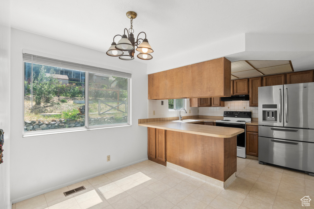 Kitchen with stainless steel fridge, white range with electric stovetop, under cabinet range hood, light countertops, and a peninsula