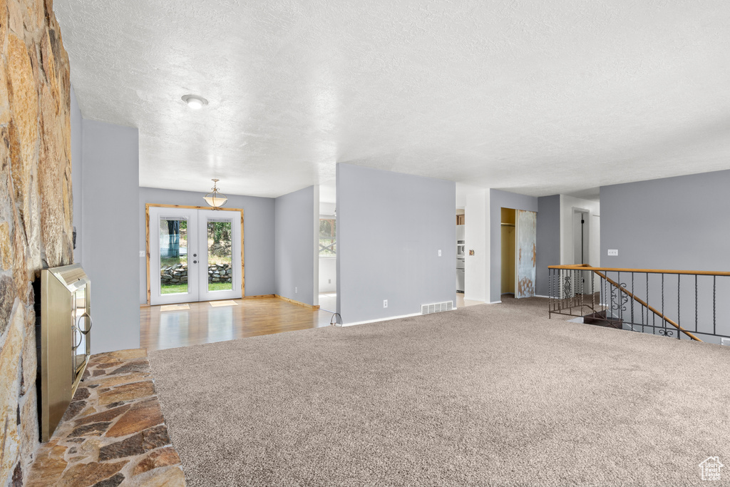 Unfurnished living room featuring a textured ceiling, carpet, and french doors
