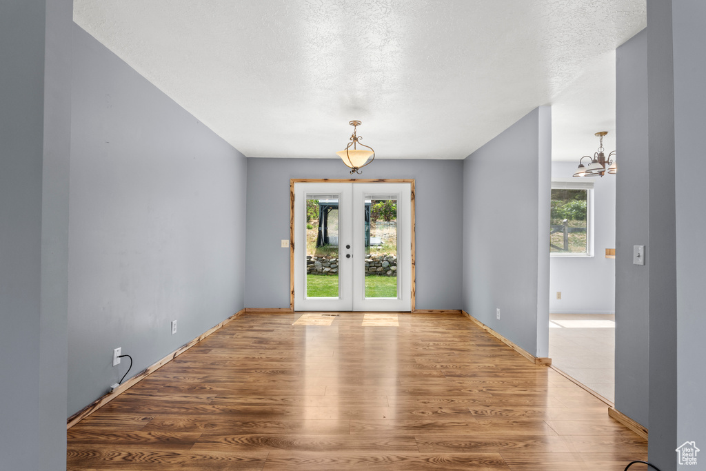Empty room with plenty of natural light, wood finished floors, a chandelier, french doors, and a textured ceiling