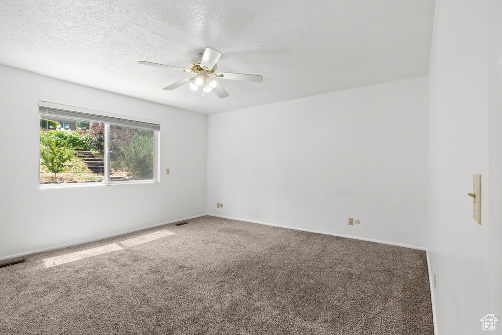 Carpeted empty room with a ceiling fan and a textured ceiling