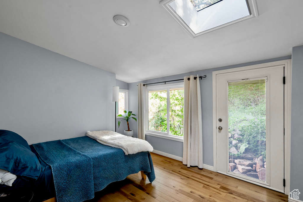 Bedroom with light wood-style flooring, lofted ceiling, a skylight, and access to outside
