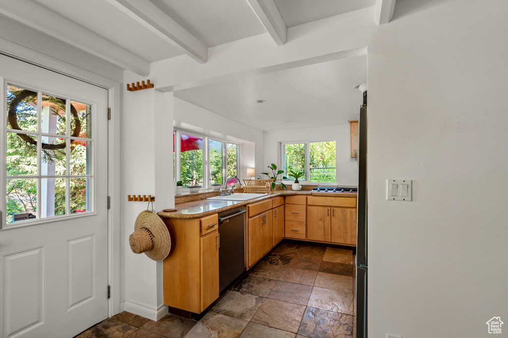 Kitchen featuring appliances with stainless steel finishes, beam ceiling, stone tile flooring, and light countertops