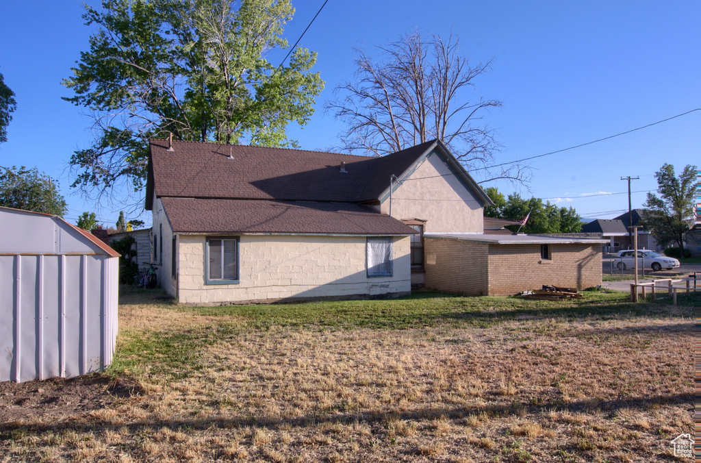 Rear view of house with a shingled roof, concrete block siding, a yard, and a storage unit