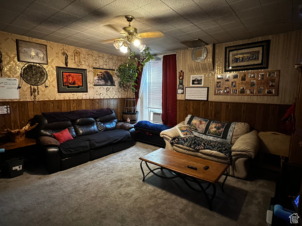 Living area with wooden walls, a wainscoted wall, a ceiling fan, and carpet flooring