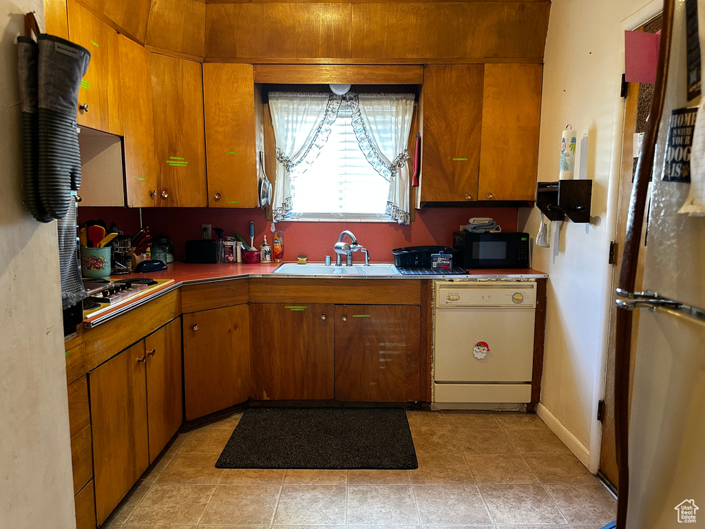 Kitchen featuring dishwasher, cooktop, black microwave, freestanding refrigerator, and brown cabinetry