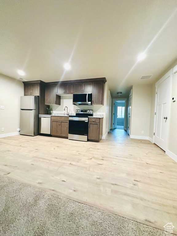 Kitchen with stainless steel appliances, light countertops, dark brown cabinets, and light wood-type flooring