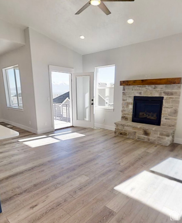 Unfurnished living room featuring plenty of natural light, a ceiling fan, lofted ceiling, wood finished floors, and a fireplace