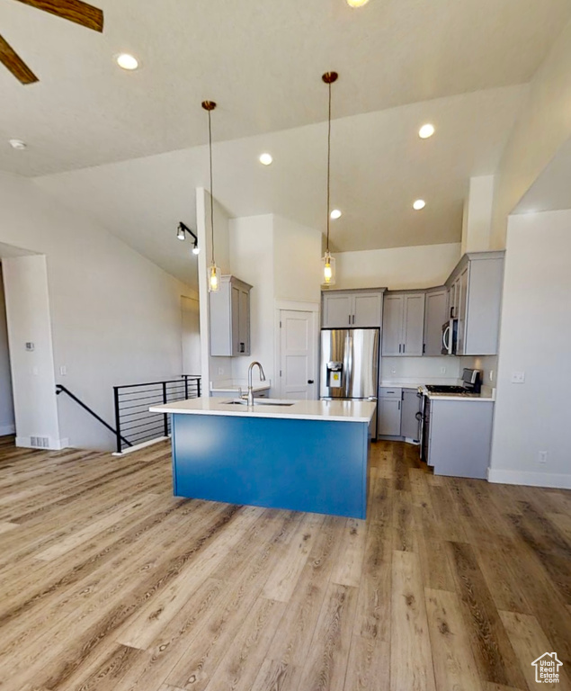 Kitchen featuring appliances with stainless steel finishes, gray cabinets, vaulted ceiling, light wood-type flooring, and hanging light fixtures