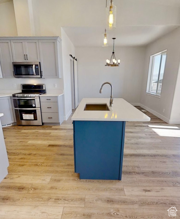 Kitchen featuring stainless steel appliances, gray cabinets, light wood-style floors, and light countertops