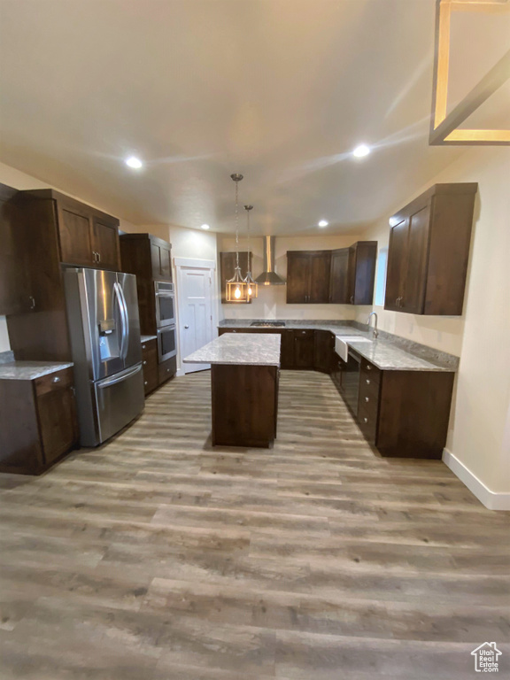 Kitchen with stainless steel appliances, wall chimney range hood, light wood-style flooring, recessed lighting, and a kitchen island