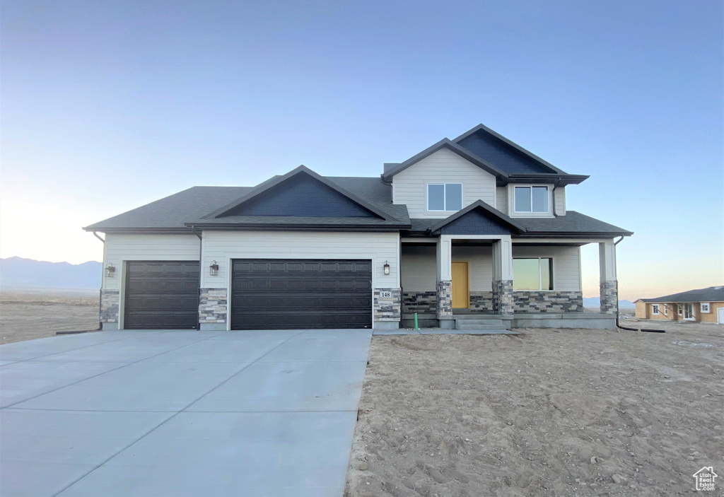 Craftsman-style house featuring an attached garage, a porch, driveway, and stone siding