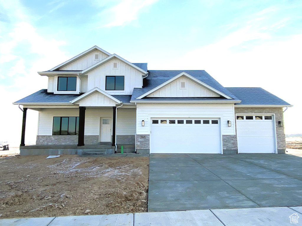 View of front facade with stone siding, a porch, driveway, and an attached garage