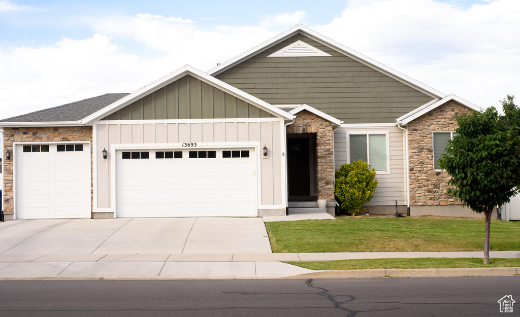 Craftsman-style house featuring stone siding, an attached garage, a front yard, driveway, and board and batten siding