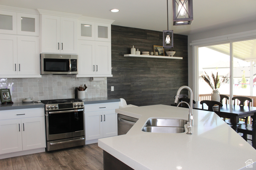 Kitchen with appliances with stainless steel finishes, a kitchen island with sink, white cabinetry, hanging light fixtures, and tasteful backsplash