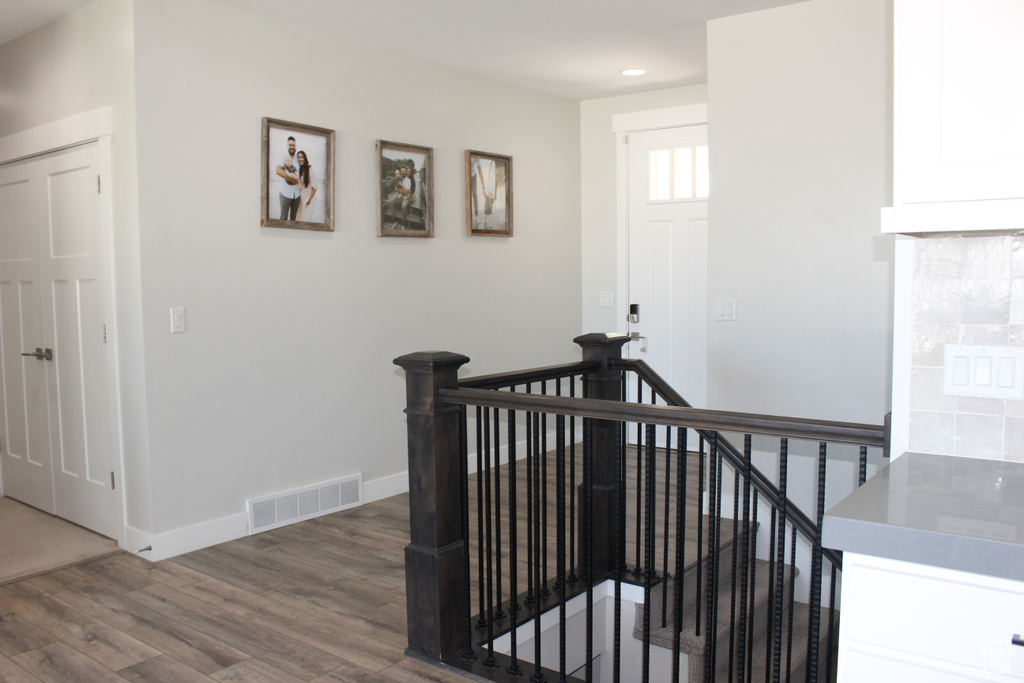 Hall with an upstairs landing, wood finished floors, and recessed lighting