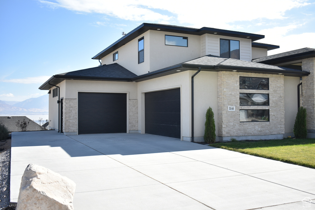 View of front facade featuring stone siding, concrete driveway, an attached garage, and stucco siding