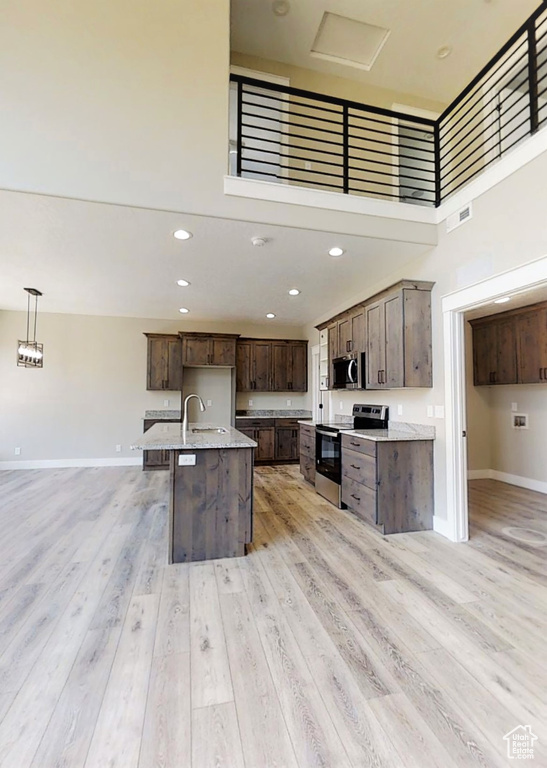 Kitchen with appliances with stainless steel finishes, open floor plan, light wood-style floors, dark brown cabinetry, and a towering ceiling
