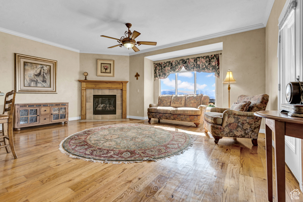 Living room with wood finished floors, ornamental molding, a ceiling fan, and a tile fireplace