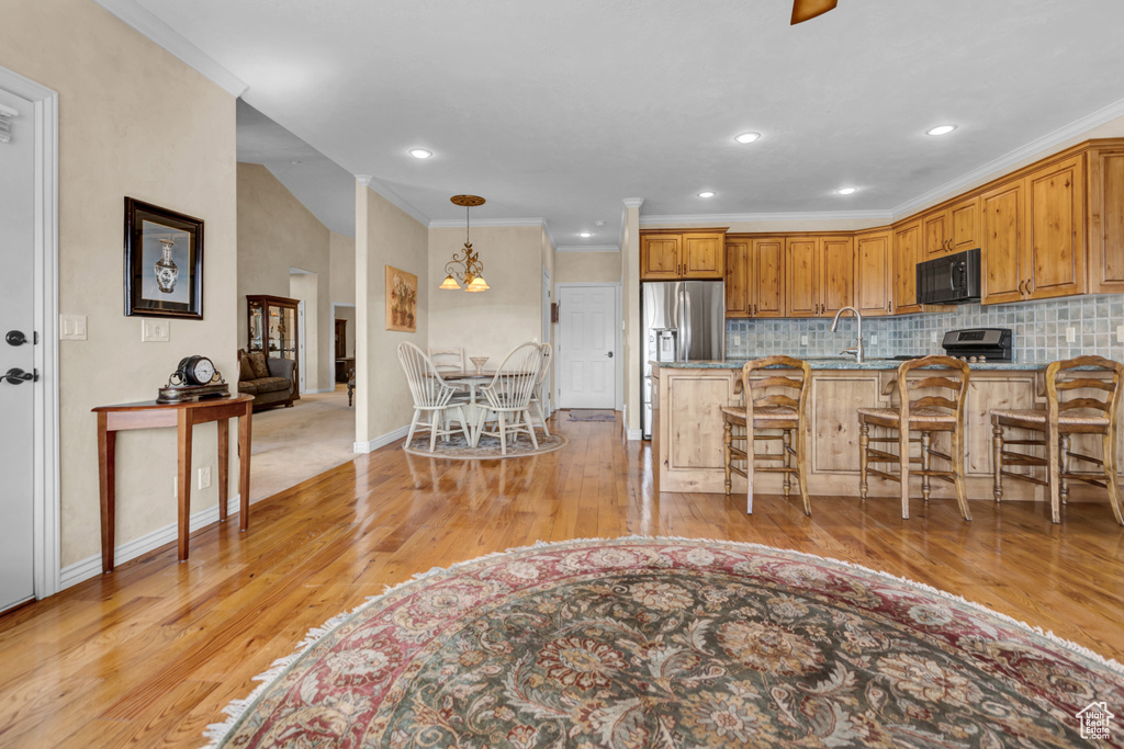 Kitchen with a breakfast bar area, black microwave, crown molding, light wood-type flooring, and a peninsula