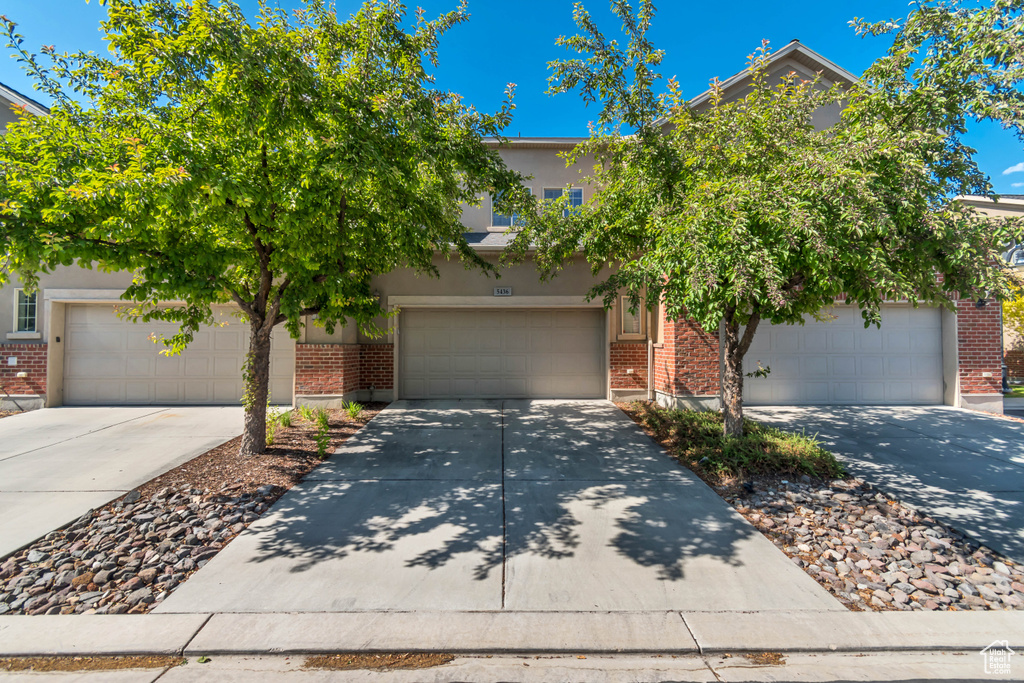 View of property hidden behind natural elements featuring brick siding, concrete driveway, a garage, and stucco siding