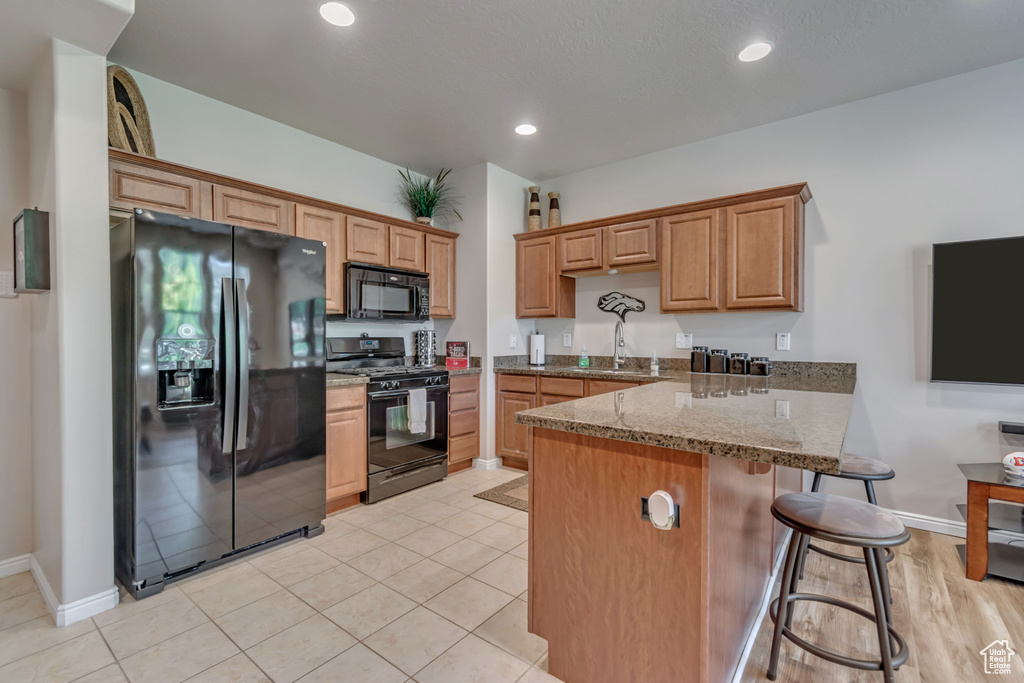 Kitchen with black appliances, a peninsula, a breakfast bar area, brown cabinets, and stone counters