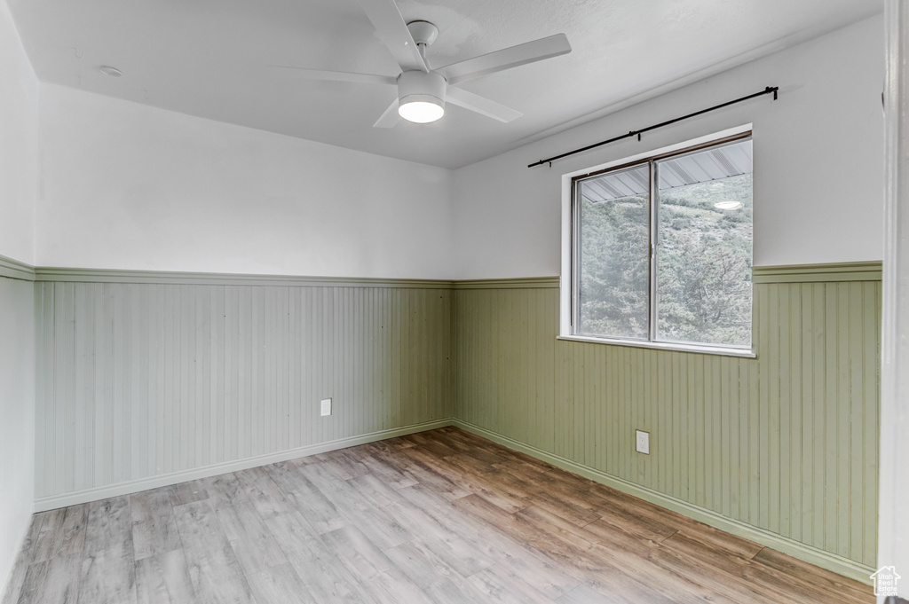 Unfurnished room featuring a wainscoted wall, wood finished floors, and a ceiling fan