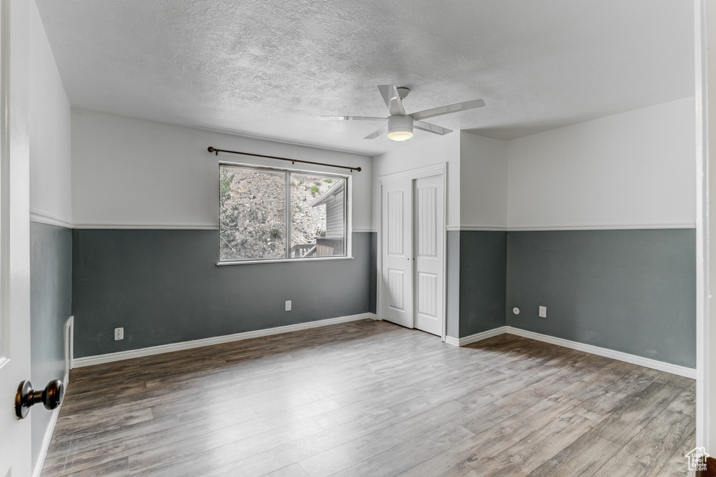 Unfurnished bedroom with wood finished floors, a closet, a textured ceiling, and ceiling fan