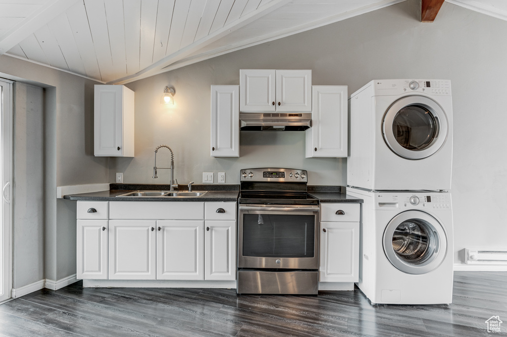 Kitchen with electric range, range hood, stacked washer and clothes dryer, dark countertops, and dark wood-style flooring