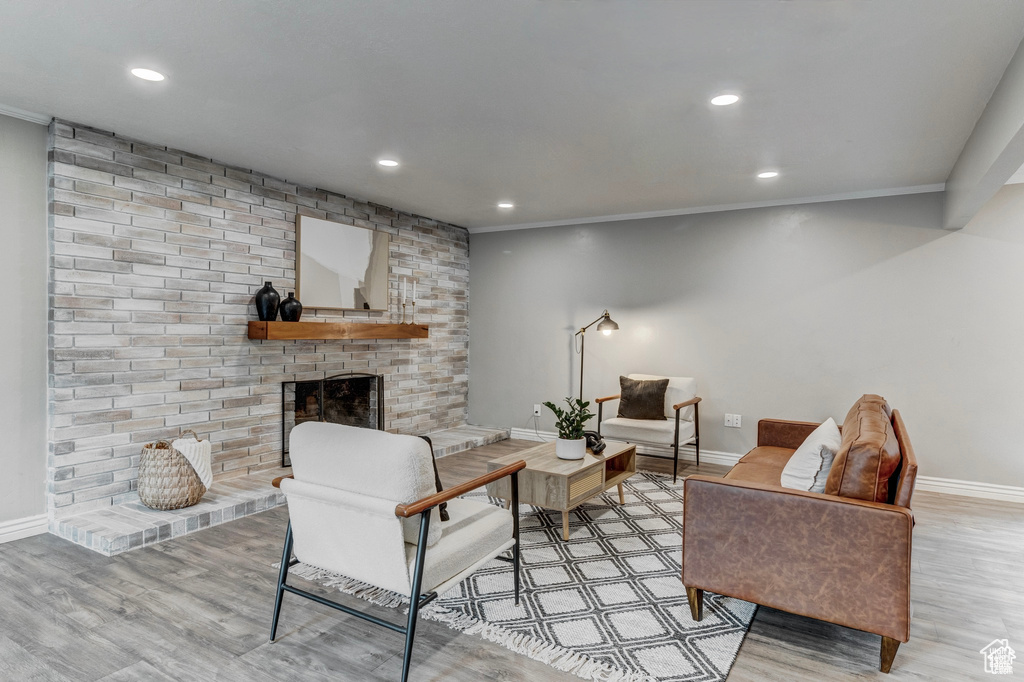 Living area featuring wood finished floors, recessed lighting, a brick fireplace, and crown molding