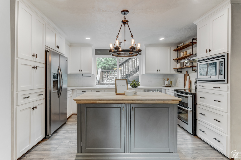 Kitchen featuring stainless steel appliances, a chandelier, wood counters, open shelves, and a center island