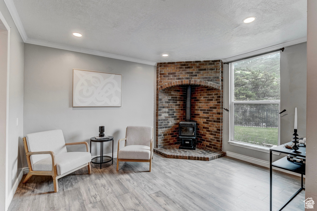 Sitting room featuring a wood stove, wood finished floors, healthy amount of natural light, a textured ceiling, and crown molding