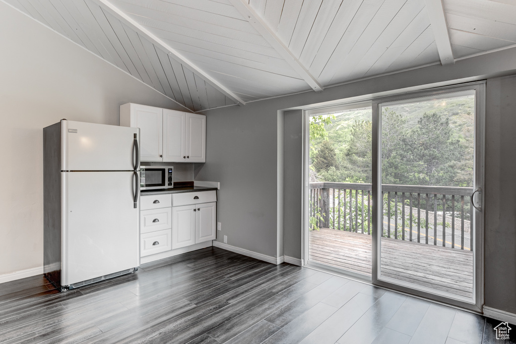 Kitchen with freestanding refrigerator, stainless steel microwave, wood ceiling, white cabinets, and dark wood-style floors