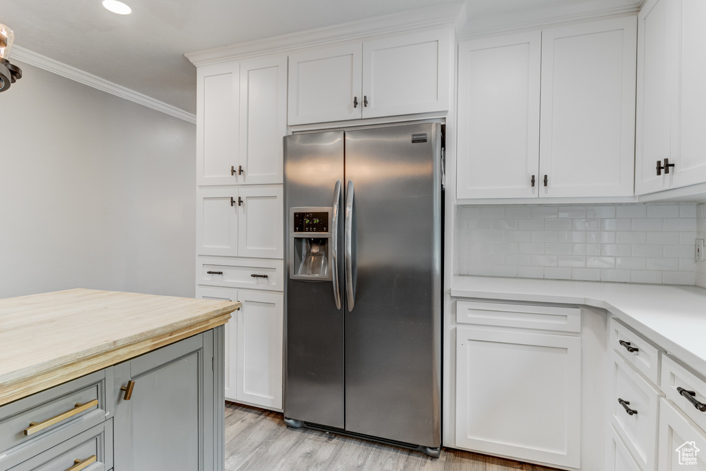 Kitchen featuring stainless steel fridge with ice dispenser, decorative backsplash, crown molding, white cabinets, and light wood-type flooring