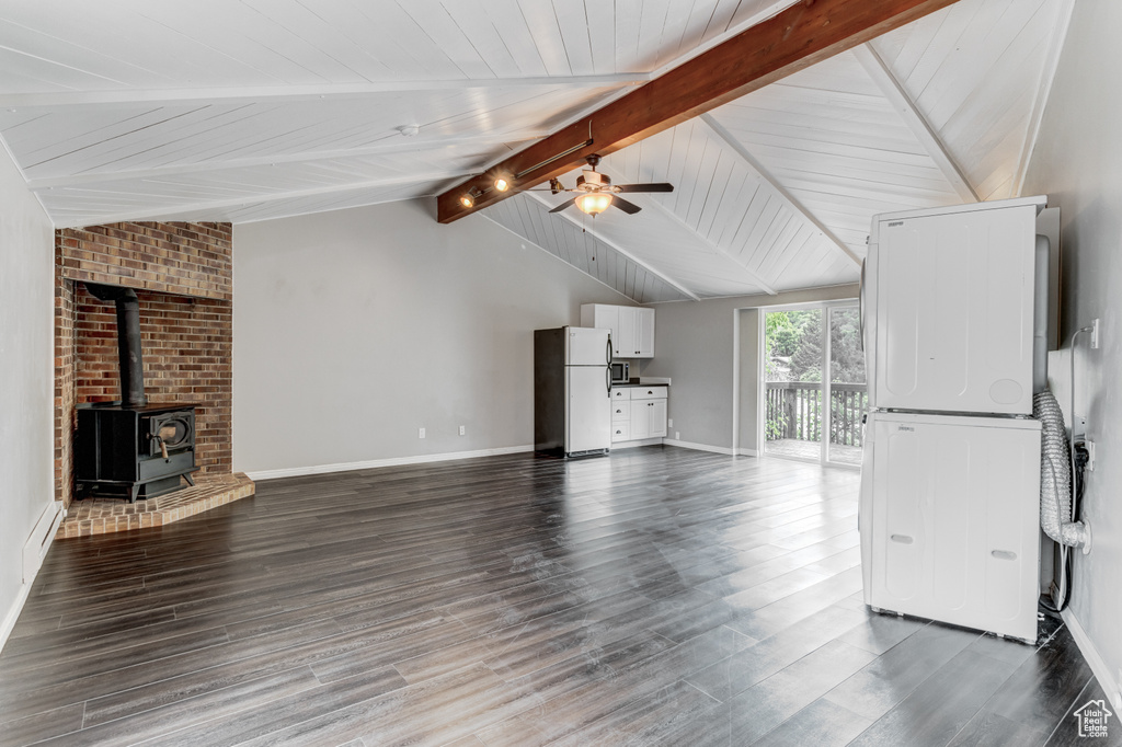 Unfurnished living room featuring a ceiling fan, a wood stove, stacked washer / drying machine, and dark wood finished floors