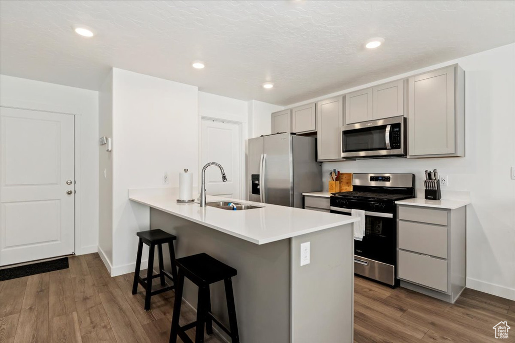 Kitchen with appliances with stainless steel finishes, gray cabinetry, a kitchen bar, dark wood-style flooring, and recessed lighting