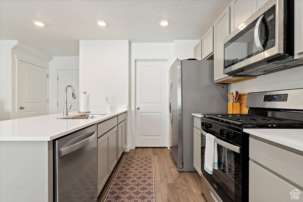 Kitchen with appliances with stainless steel finishes, a peninsula, light wood-style floors, light countertops, and recessed lighting