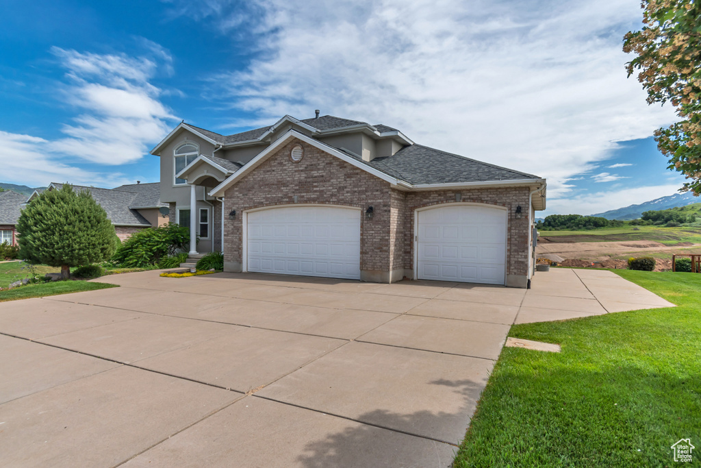 View of front facade with a garage, driveway, a front lawn, and brick siding