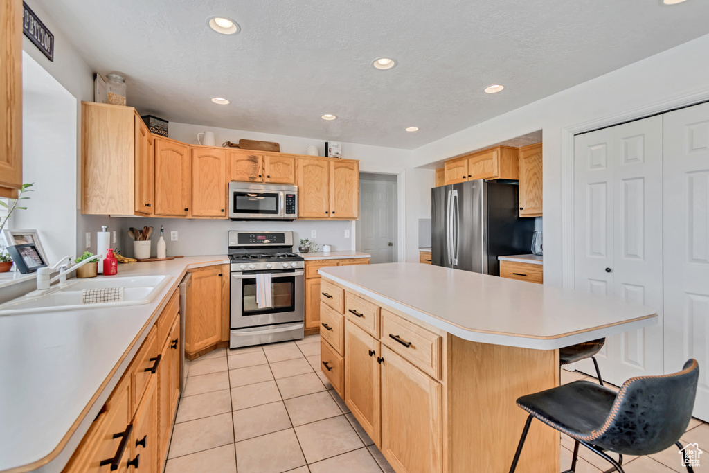 Kitchen featuring stainless steel appliances, a kitchen island, light tile patterned flooring, light countertops, and a kitchen bar