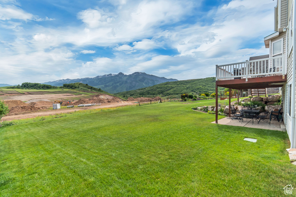 View of grassy yard with a patio and a deck with mountain view