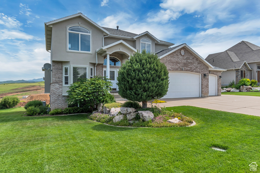 View of front of property featuring a garage, brick siding, a front lawn, and driveway