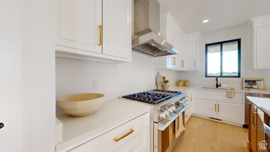 Kitchen with wall chimney range hood, range with gas stovetop, light countertops, white cabinets, and recessed lighting