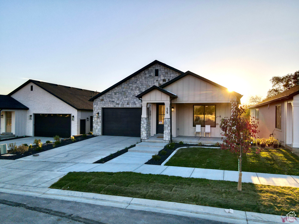 View of front of home featuring an attached garage, a lawn, driveway, covered porch, and stone siding