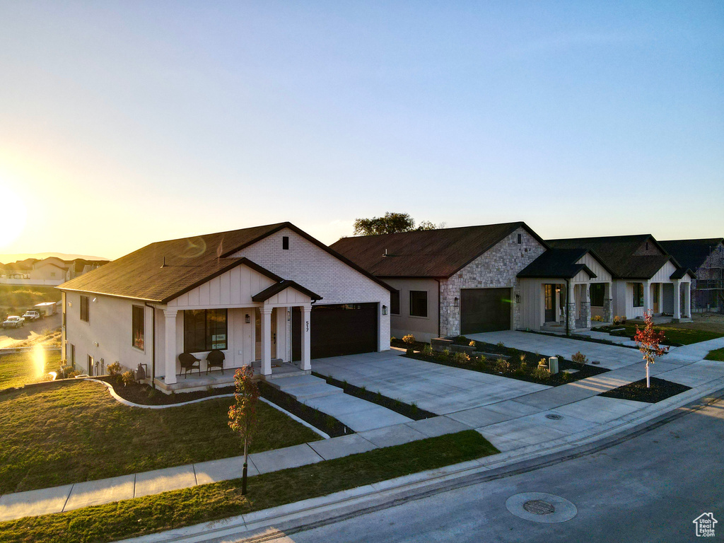 Modern farmhouse featuring concrete driveway, a garage, board and batten siding, a porch, and a lawn