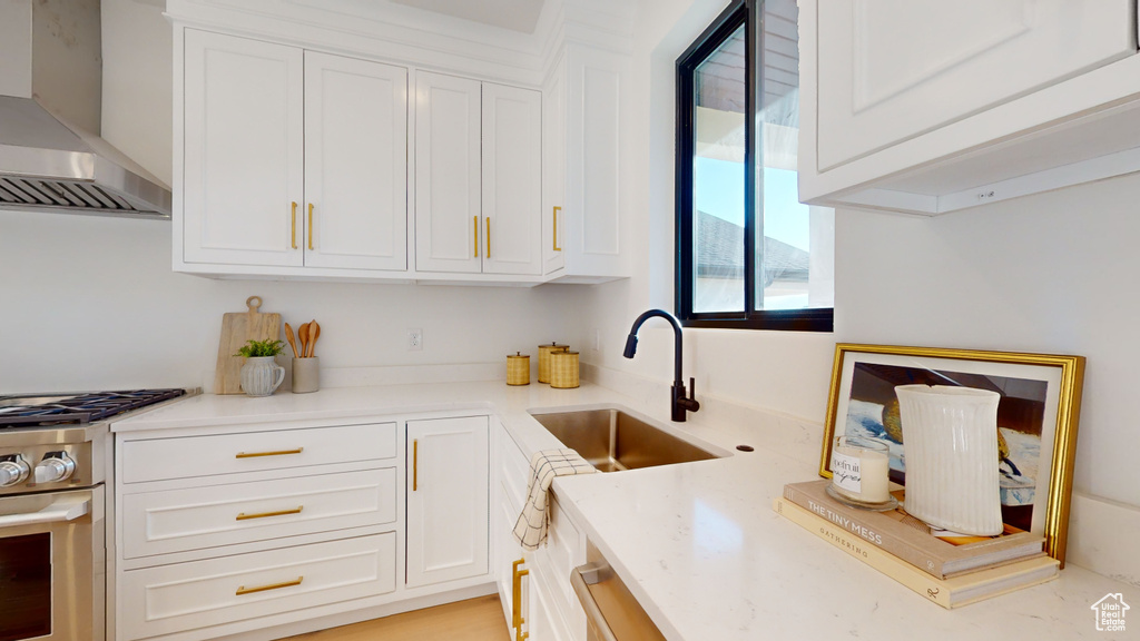 Kitchen with wall chimney range hood, gas range, and white cabinets